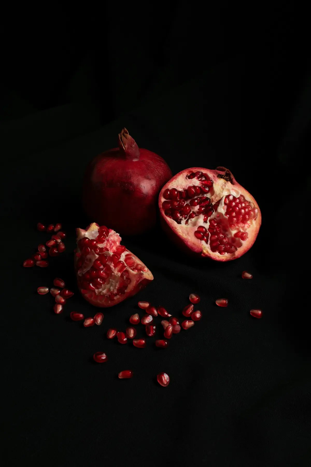 Whole and opened pomegranates showing red arils, on a dark ground