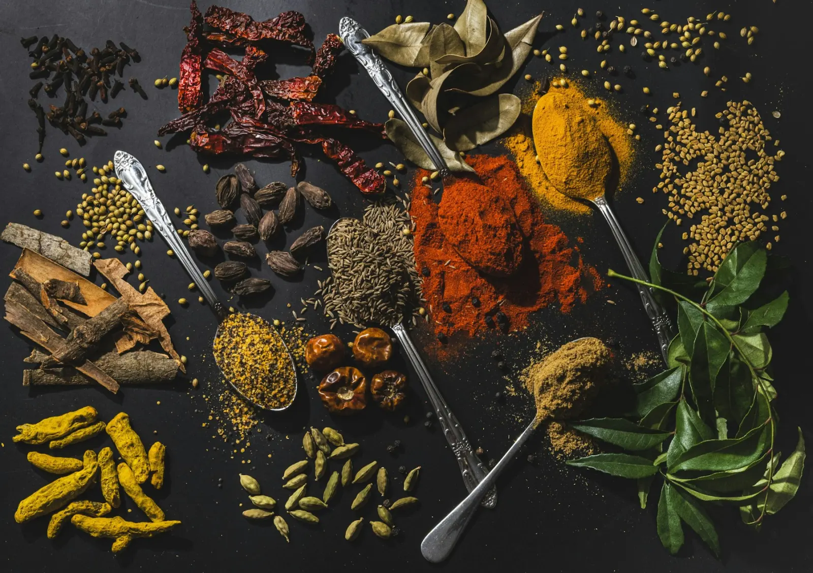 Whole and ground Indian spices, including turmeric, dry red chilli and cardamom, on a dark surface